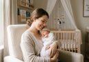 A smiling mother holding her swaddled newborn baby in a nursery for mombabyguide.com