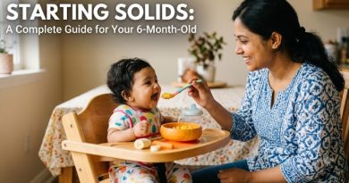 A South Asian mother smiling and feeding her 6-month-old baby girl mashed food from a bowl while the baby sits in a wooden high chair, featuring the text "STARTING SOLIDS: A Complete Guide for Your 6-Month-Old.